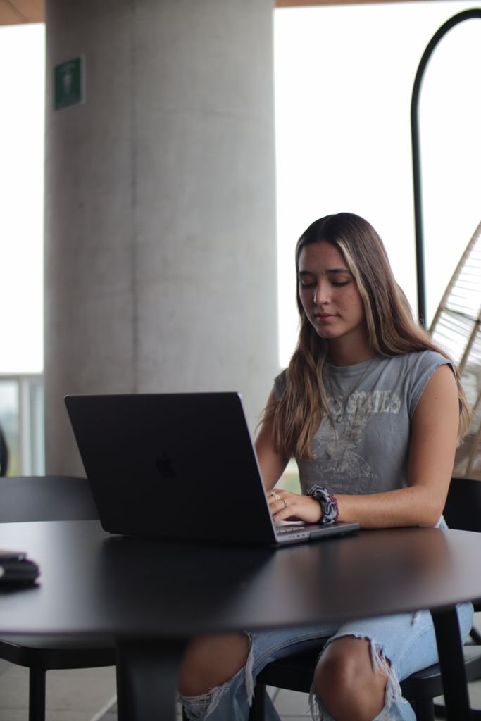 Teen girl focusing on online learning using a laptop in a modern indoor setting.